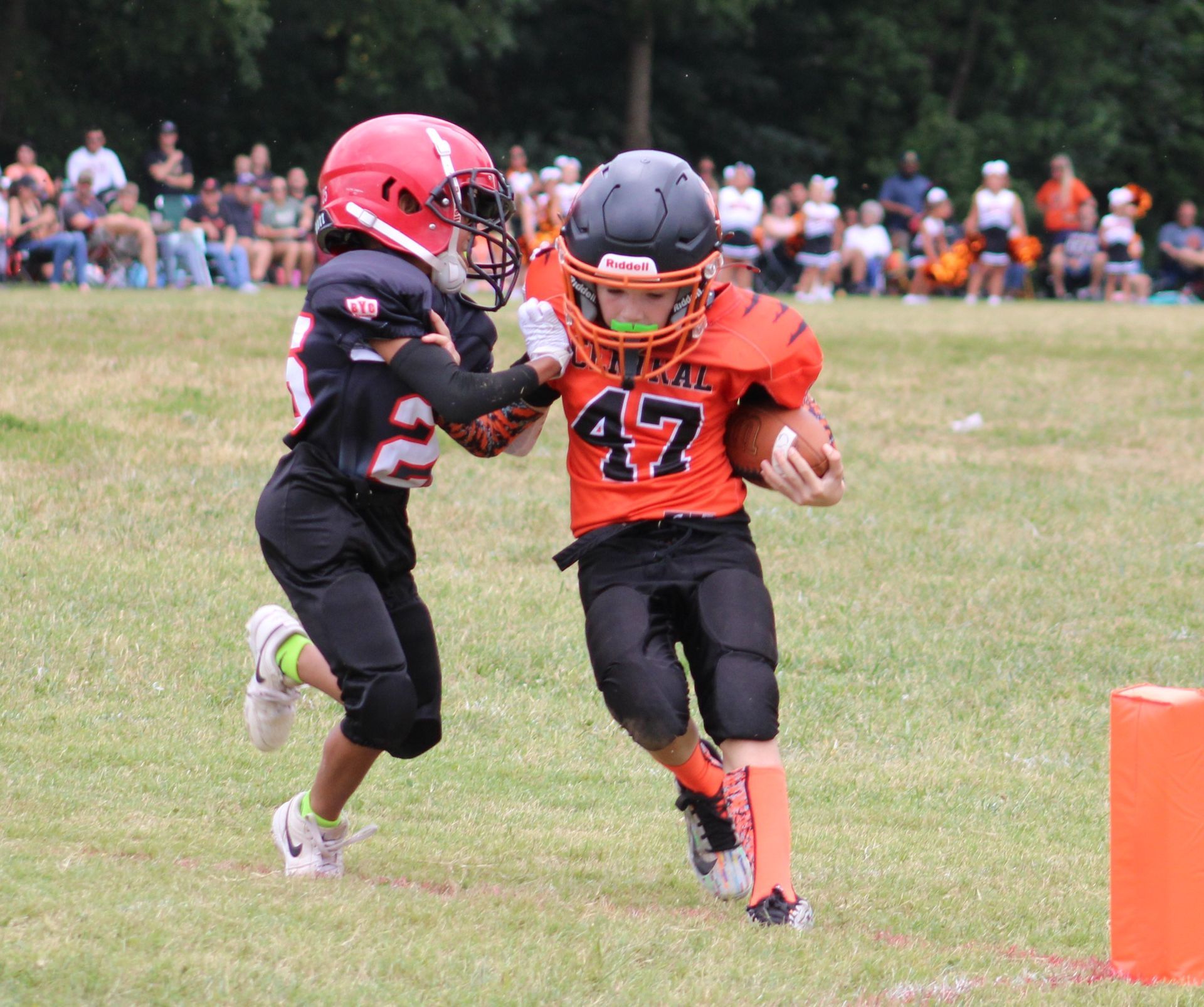 Two young football players in black and orange uniforms running on a grassy field