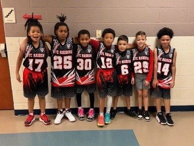Youth basketball team posing in black-and-red jerseys against a gym wall.