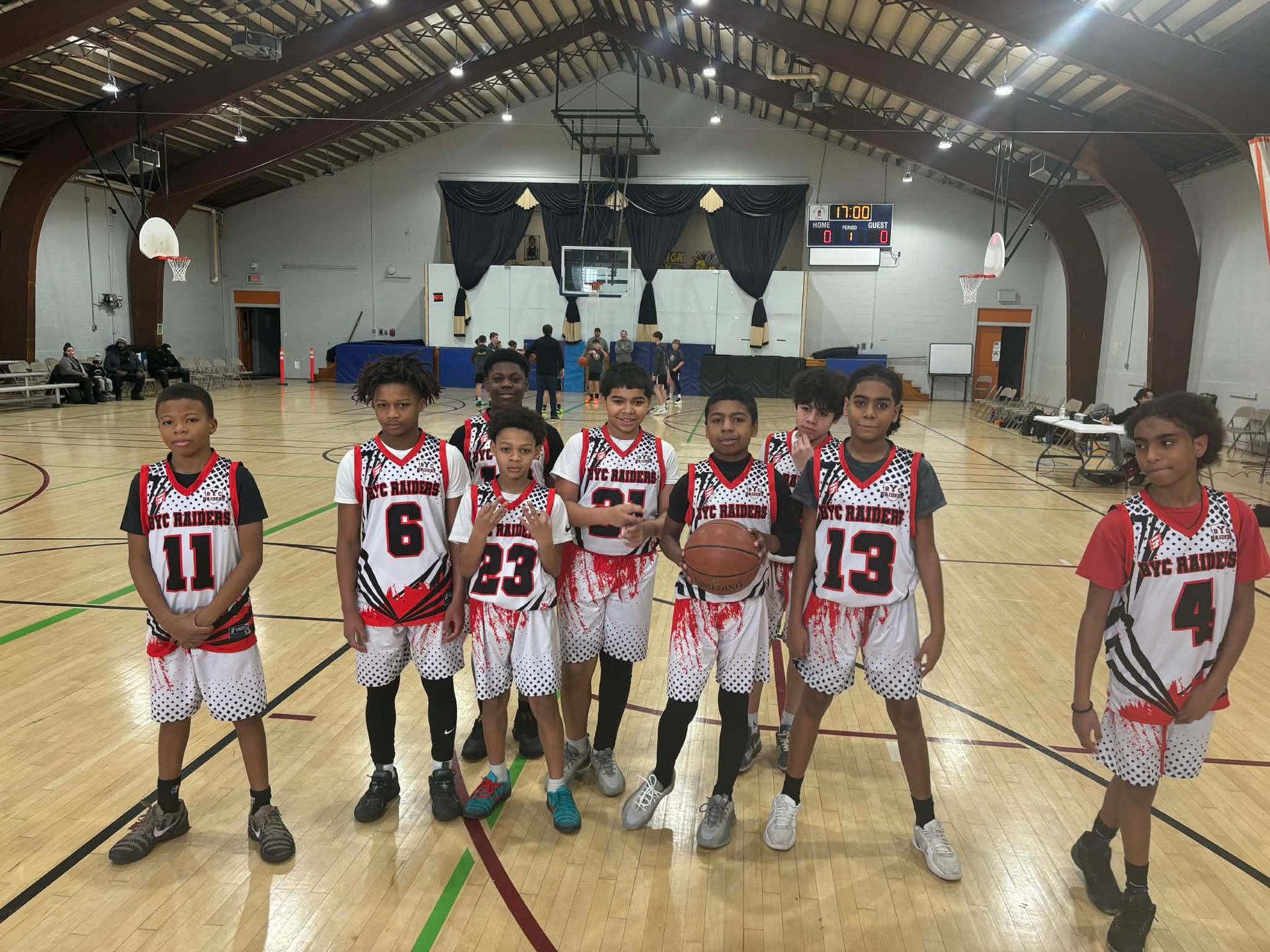 Youth basketball team posing on an indoor court, wearing red, white, and black uniforms.