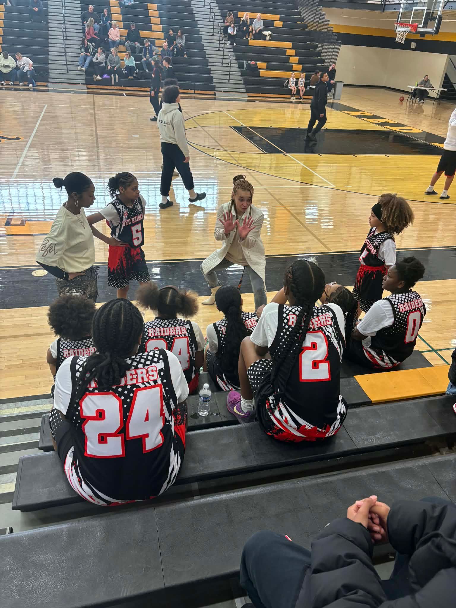 Youth basketball players sit on the bench during a game, watching the action on the court.