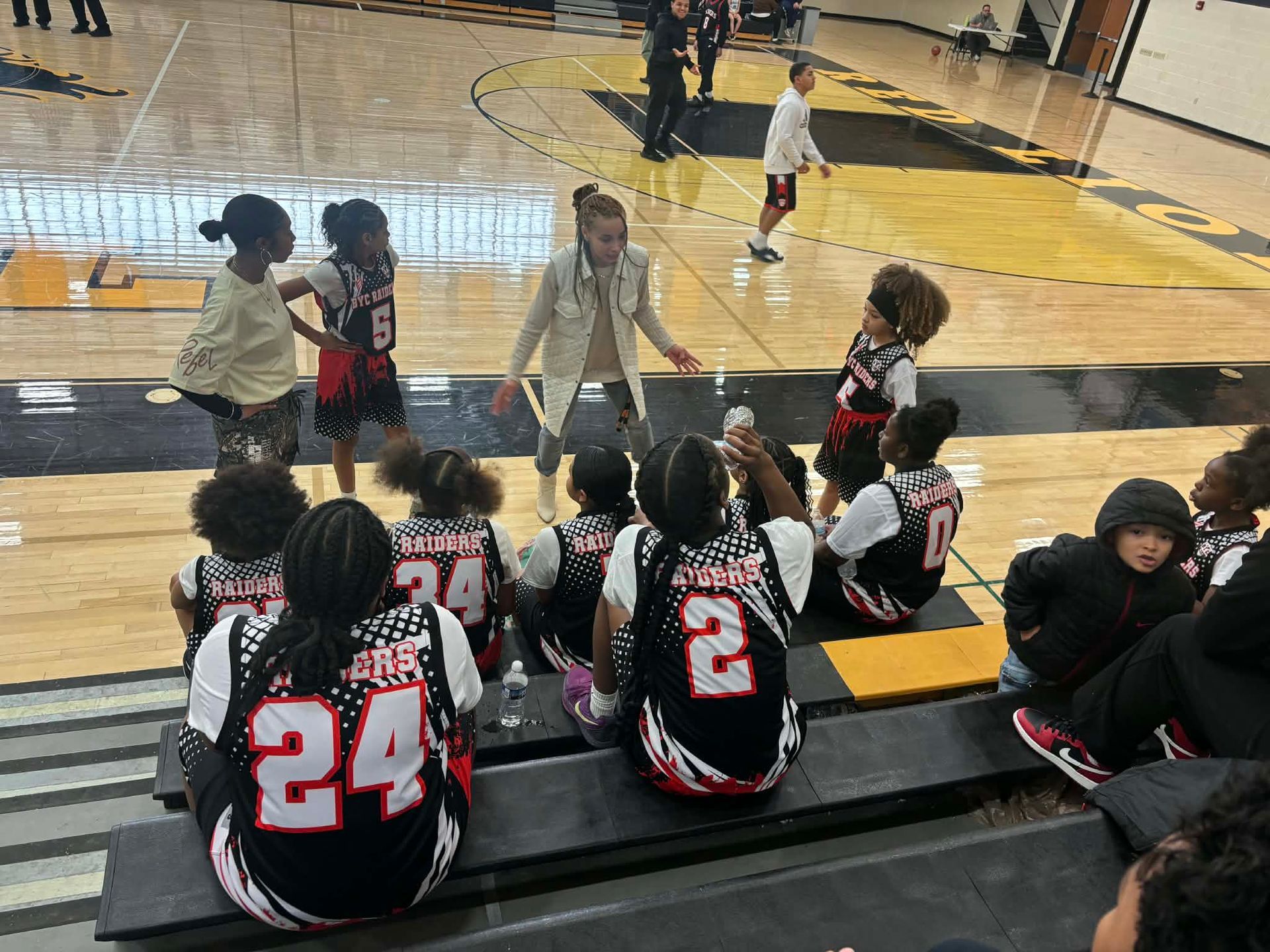 Basketball bench with players in black and red jerseys watching a game on the court