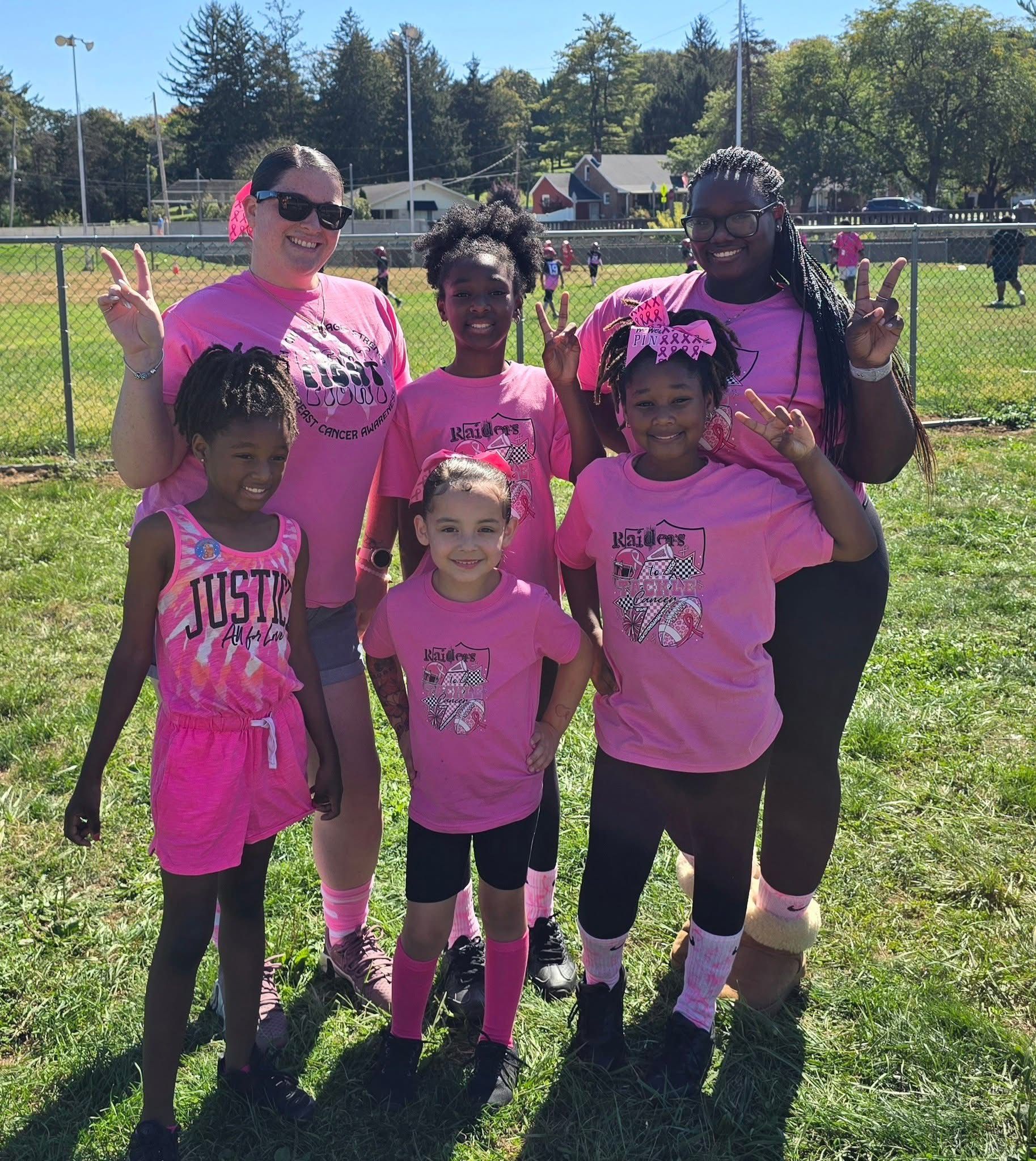 Six people in pink shirts pose together on a sunny grassy field