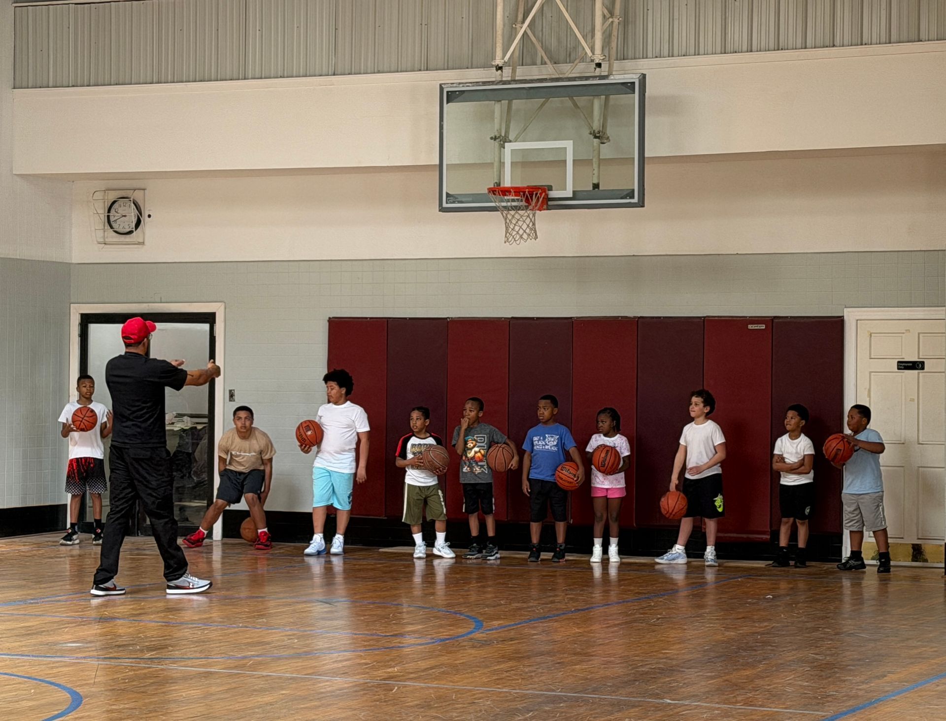 Coach instructing a line of children on an indoor basketball court beneath a hoop