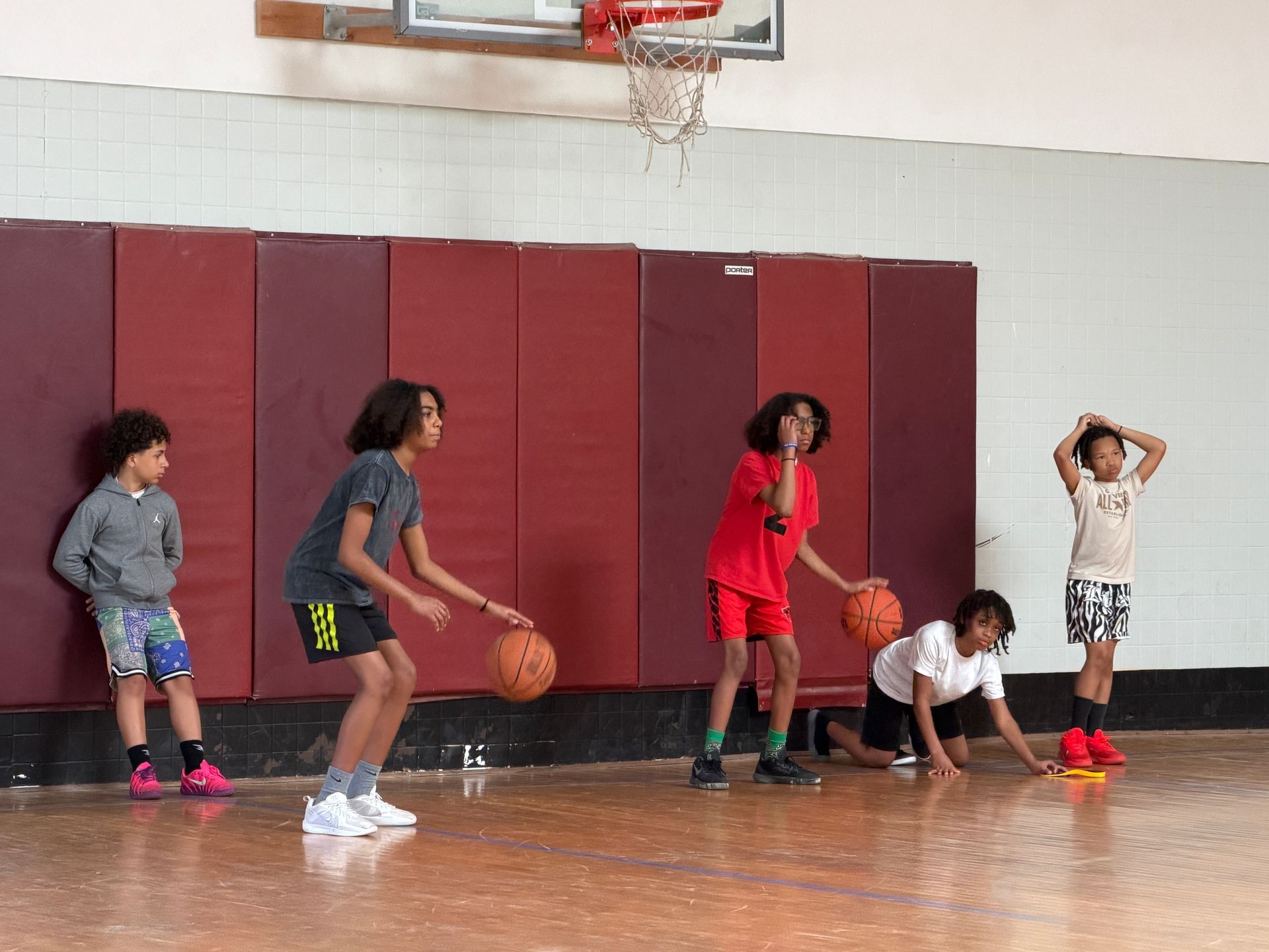 Children playing basketball in a gym, with one dribbling and others waiting nearby.