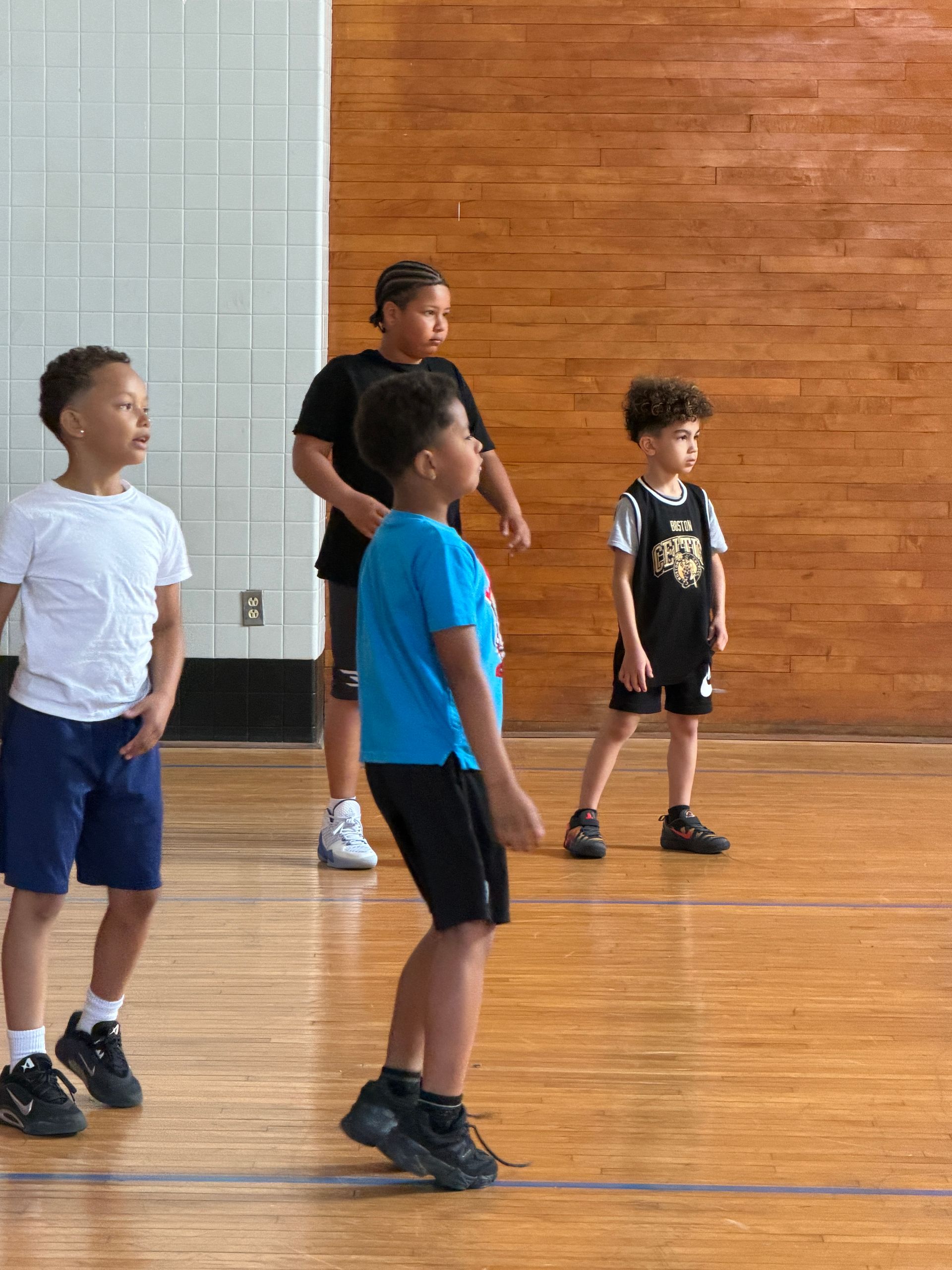 Children standing in a gymnasium, facing forward during an activity.