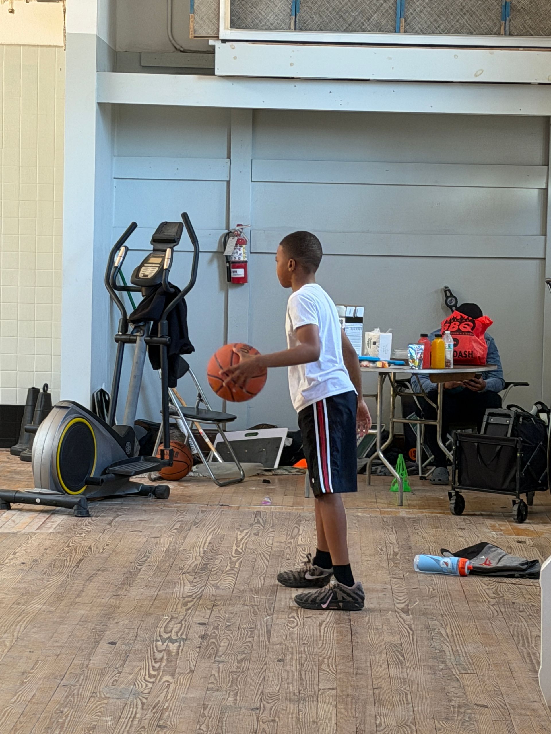 Child holding a basketball in a garage beside exercise equipment and tools