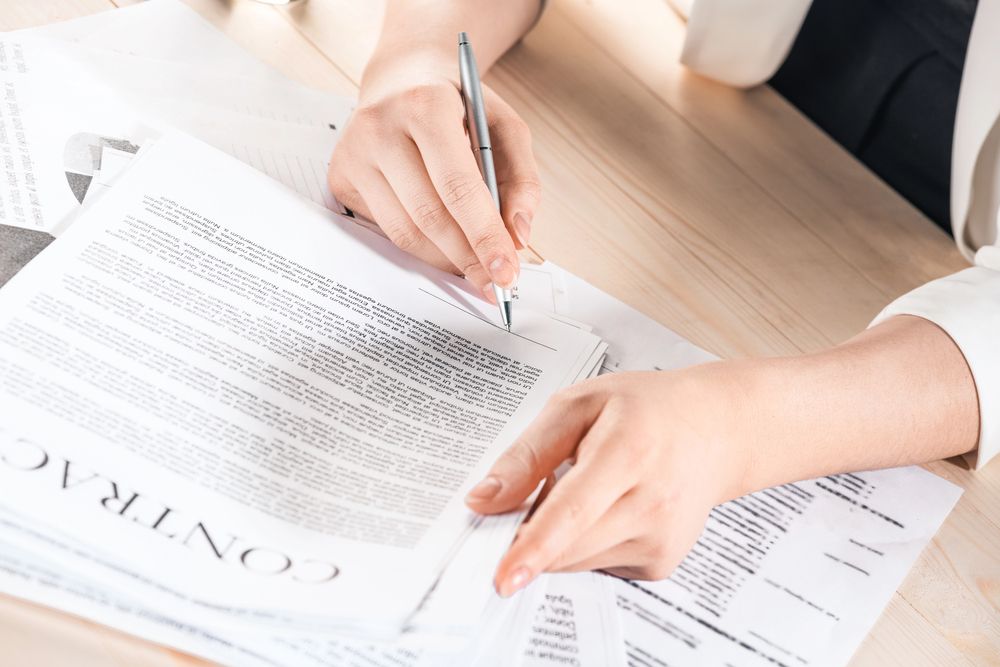 Unas manos firmando un contrato sobre unos documentos impresos en un escritorio