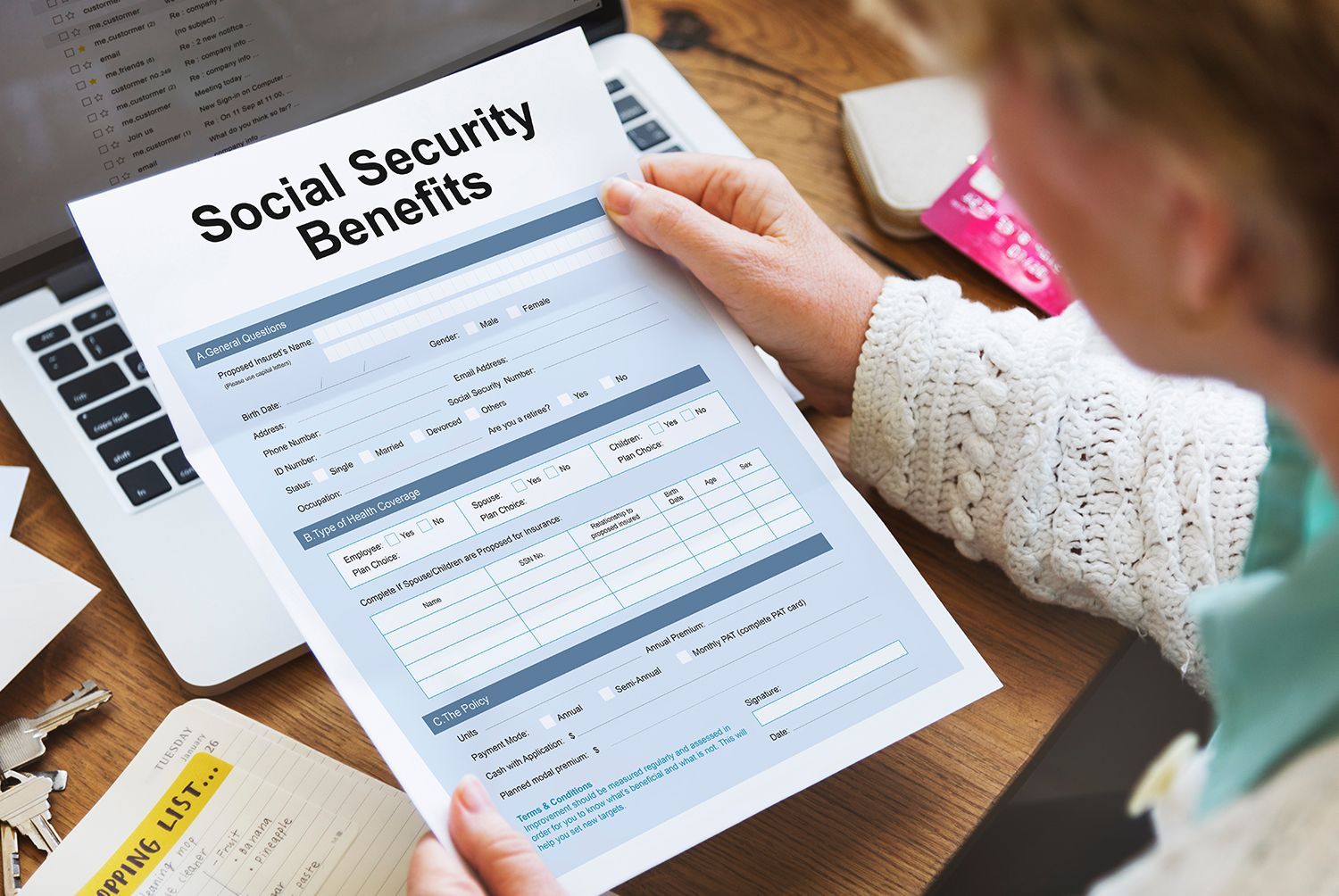 Person reviewing a Social Security benefits form at a desk with a laptop. Person reviewing a Social Security benefits form at a desk with a laptop.