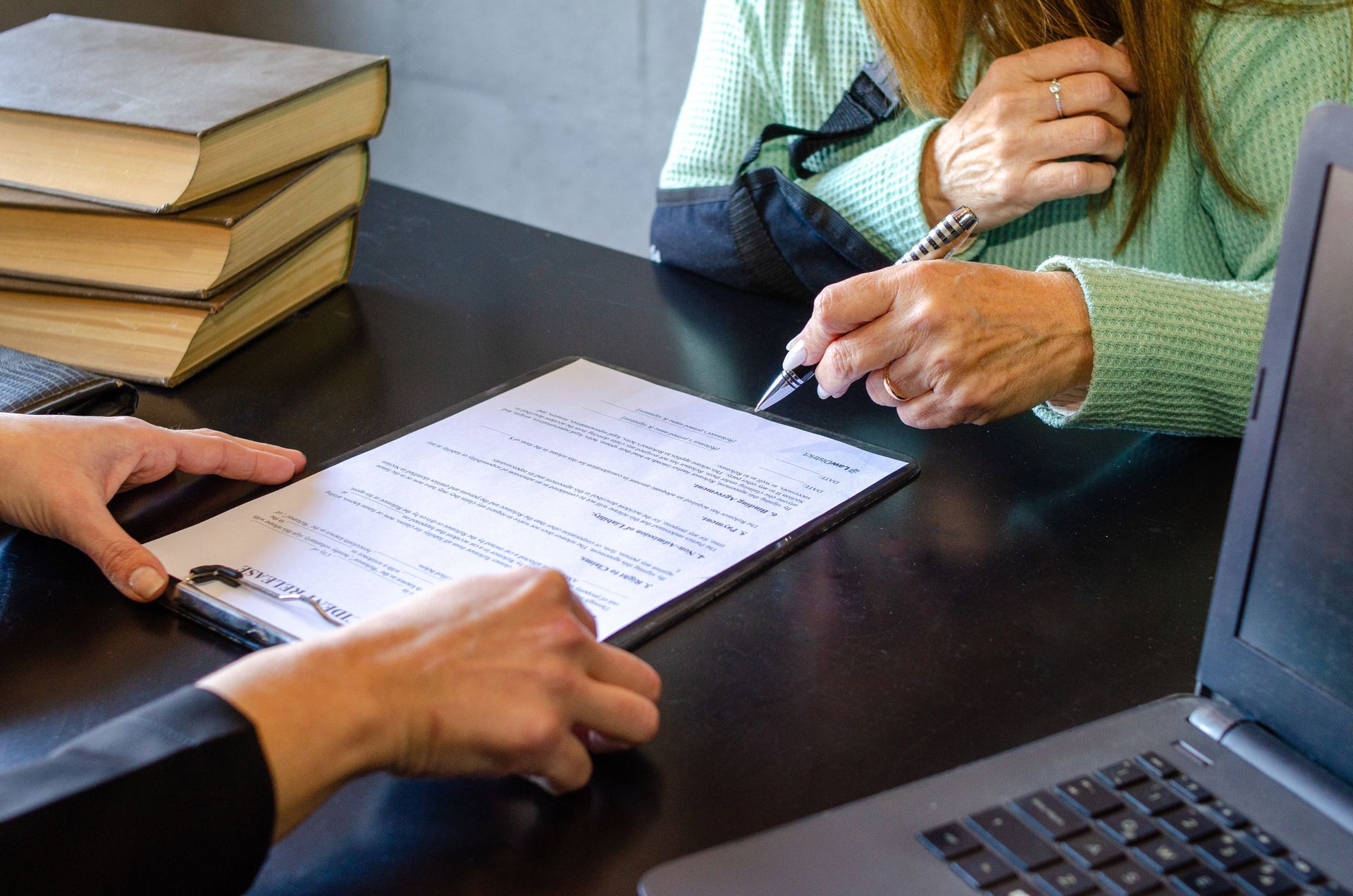 Two people review a form at a desk beside a laptop and stacked books Two people review a form at a desk beside a laptop and stacked books
