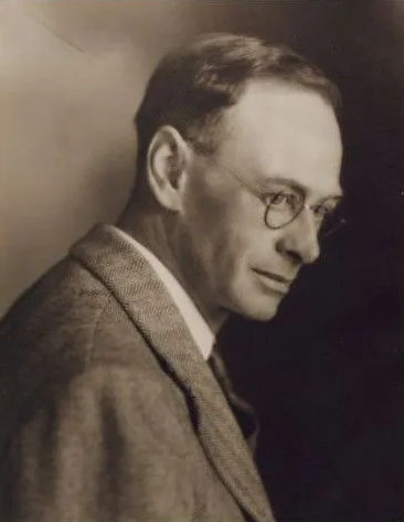 Sepia portrait of a man in glasses and a suit, shown in profile against a dark background.