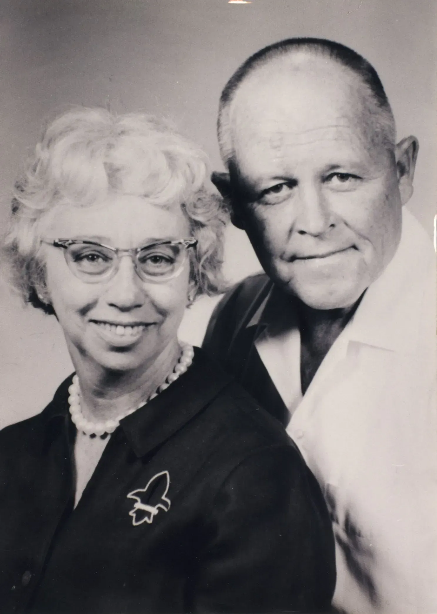 Black-and-white portrait of an older couple smiling, posed closely together against a plain background