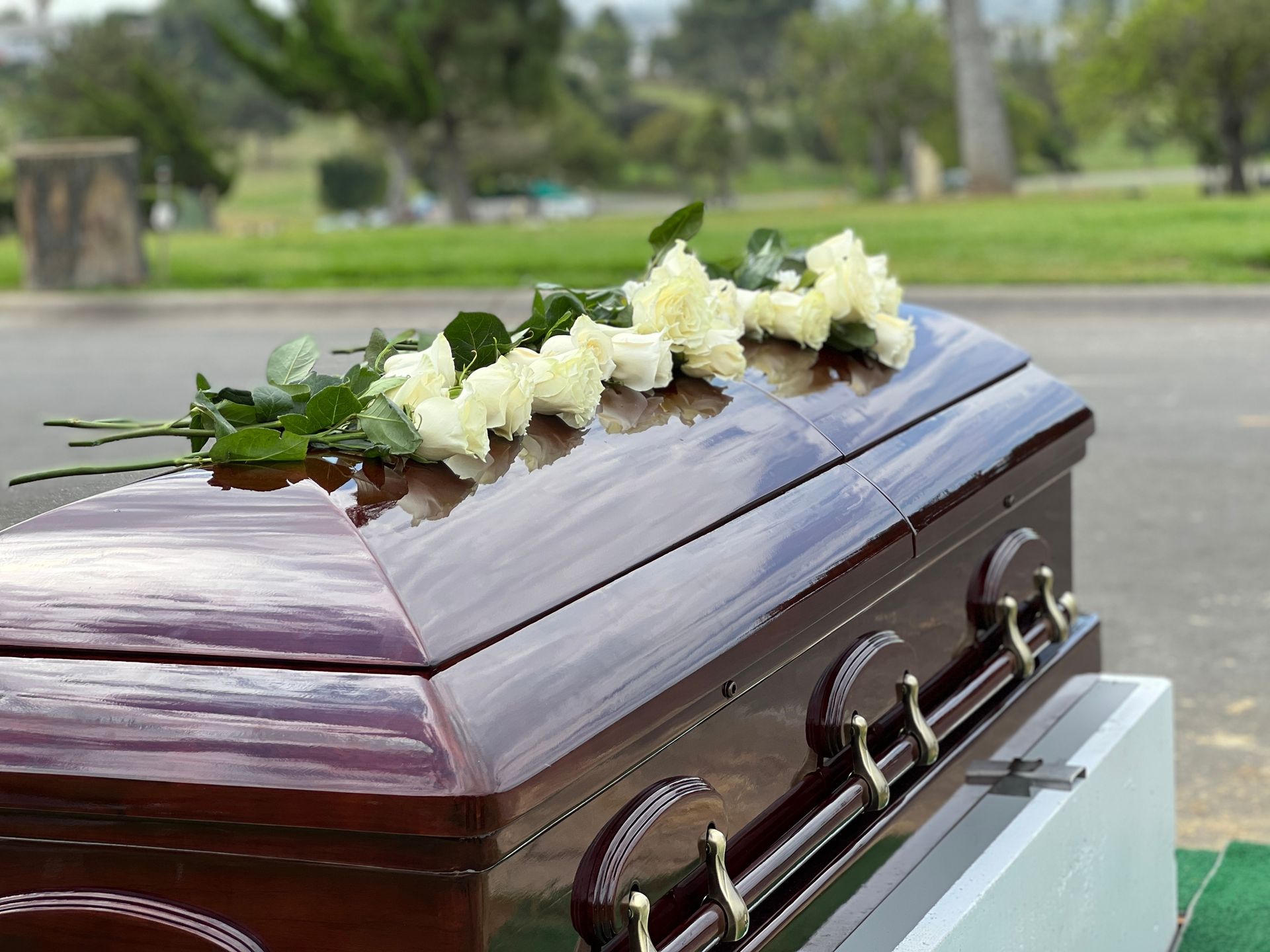 A brown casket with white flowers on top, outdoors on a roadside.