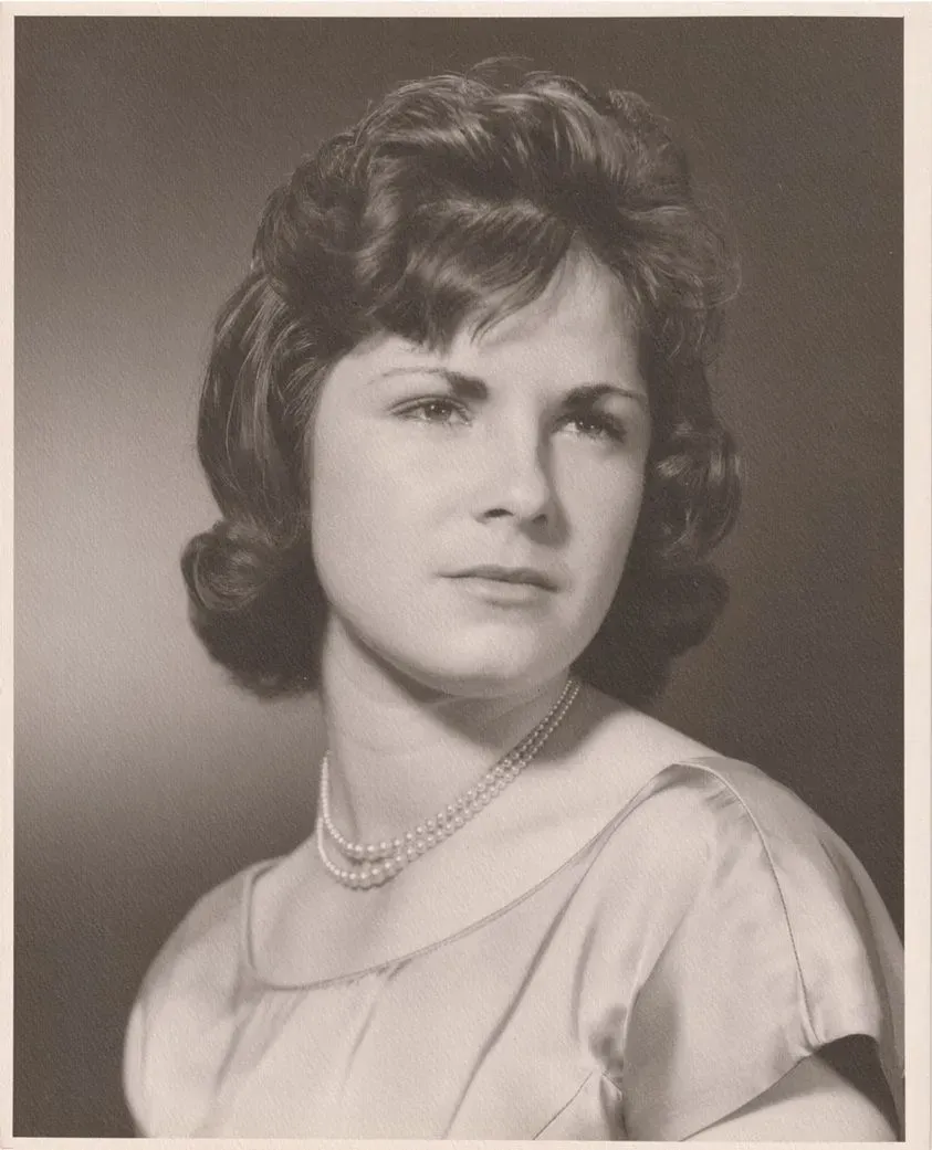 Black-and-white studio portrait of a woman in a light dress and pearl necklace, looking slightly left