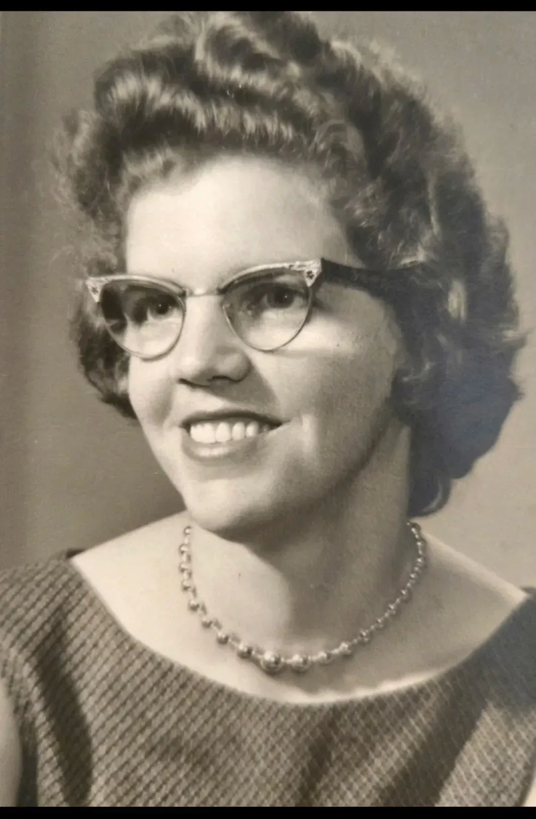 Studio portrait of a smiling woman wearing glasses, a sweater, and a beaded necklace