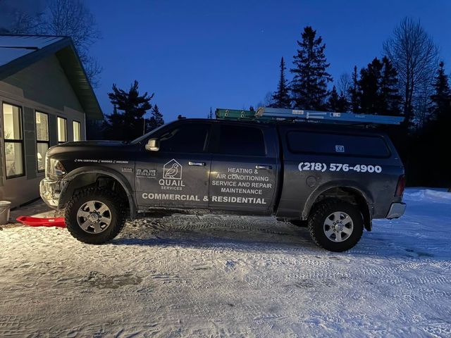 Dark work truck parked in snowy driveway beside a lit house at dusk