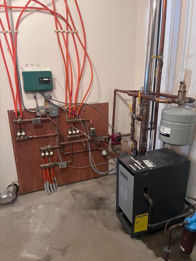Boiler room with red pipes, control panels, and a black water heater on a concrete floor