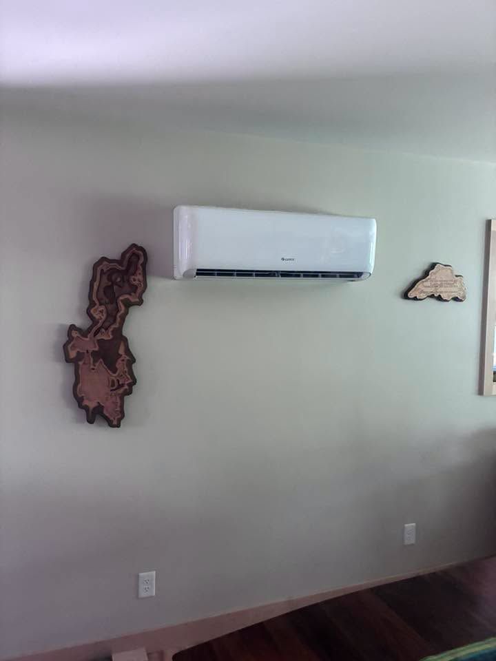 Empty wall with a white air conditioner and two wooden wall art pieces above a hardwood floor.