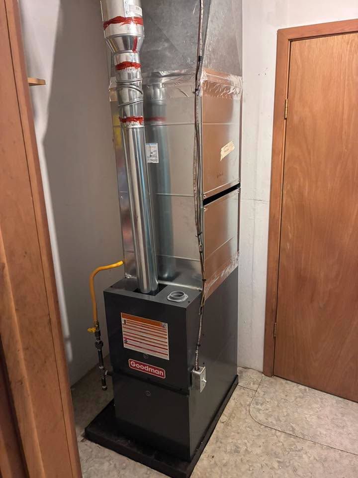 Black furnace with silver ducting in a closet beside a wooden door and tiled floor