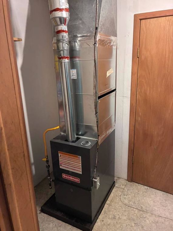 Black furnace with silver vent pipes in a narrow utility closet beside a wooden door.