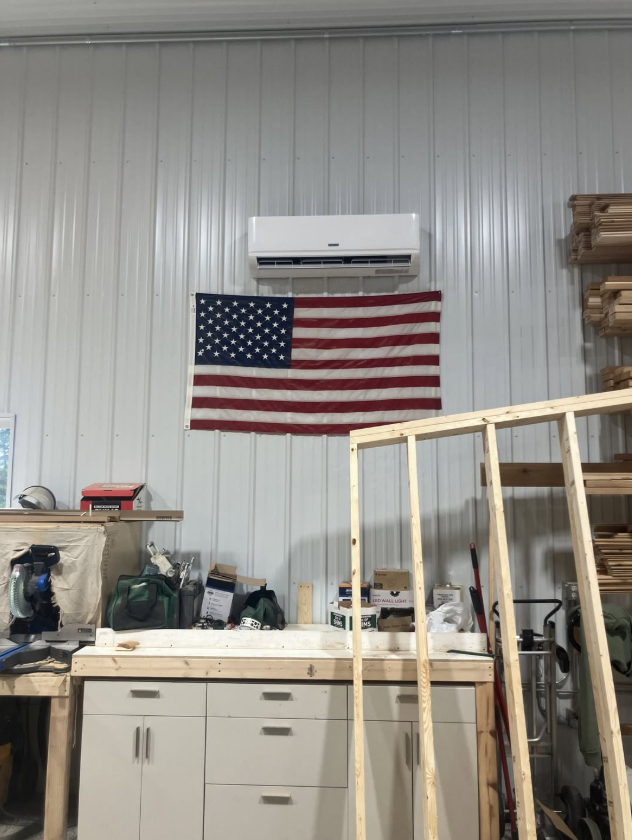 Workbench in garage with American flag on white wall and an air conditioner above it