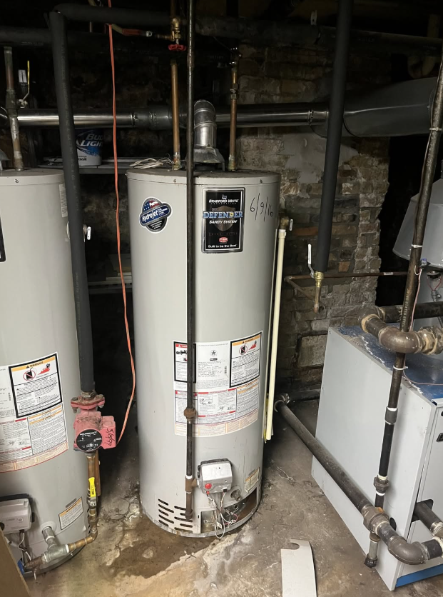 Two white water heaters in a basement utility room with exposed pipes and stone wall.