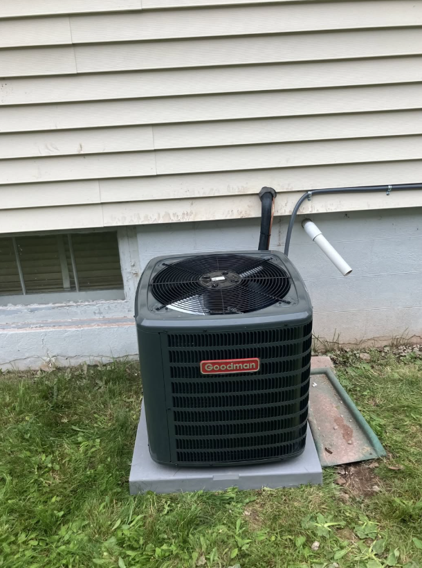 Outdoor air conditioning unit beside a house on a concrete pad, with siding and grass nearby