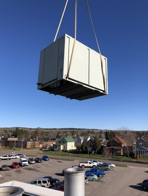 Large white crate suspended by straps above a parking lot on a clear blue day