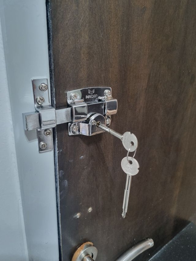 Primer plano de una puerta de madera asegurada con un pestillo de metal y dos llaves colgando de la cerradura.