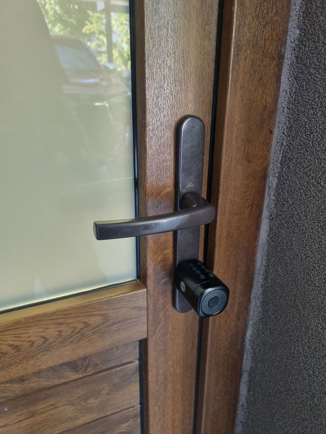 Primer plano de una manija y cerradura negras en una puerta de madera con panel de vidrio esmerilado.