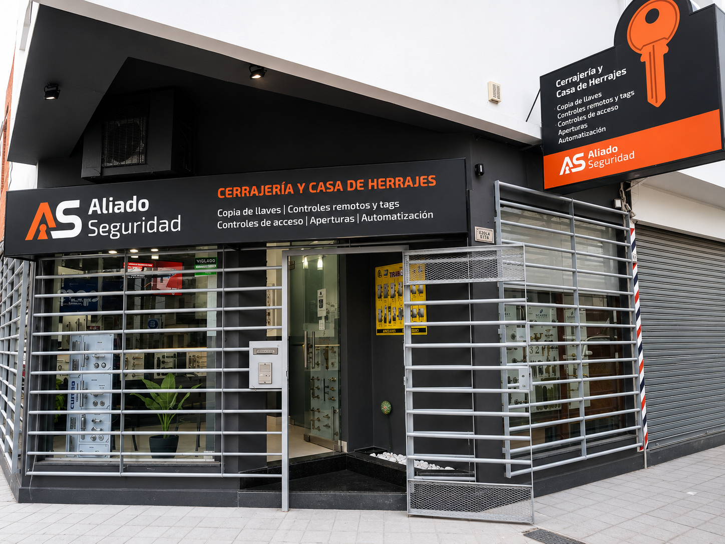 Fachada de “Alad Seguridad” con letreros negros y naranjas y rejas de seguridad metálicas en la entrada.