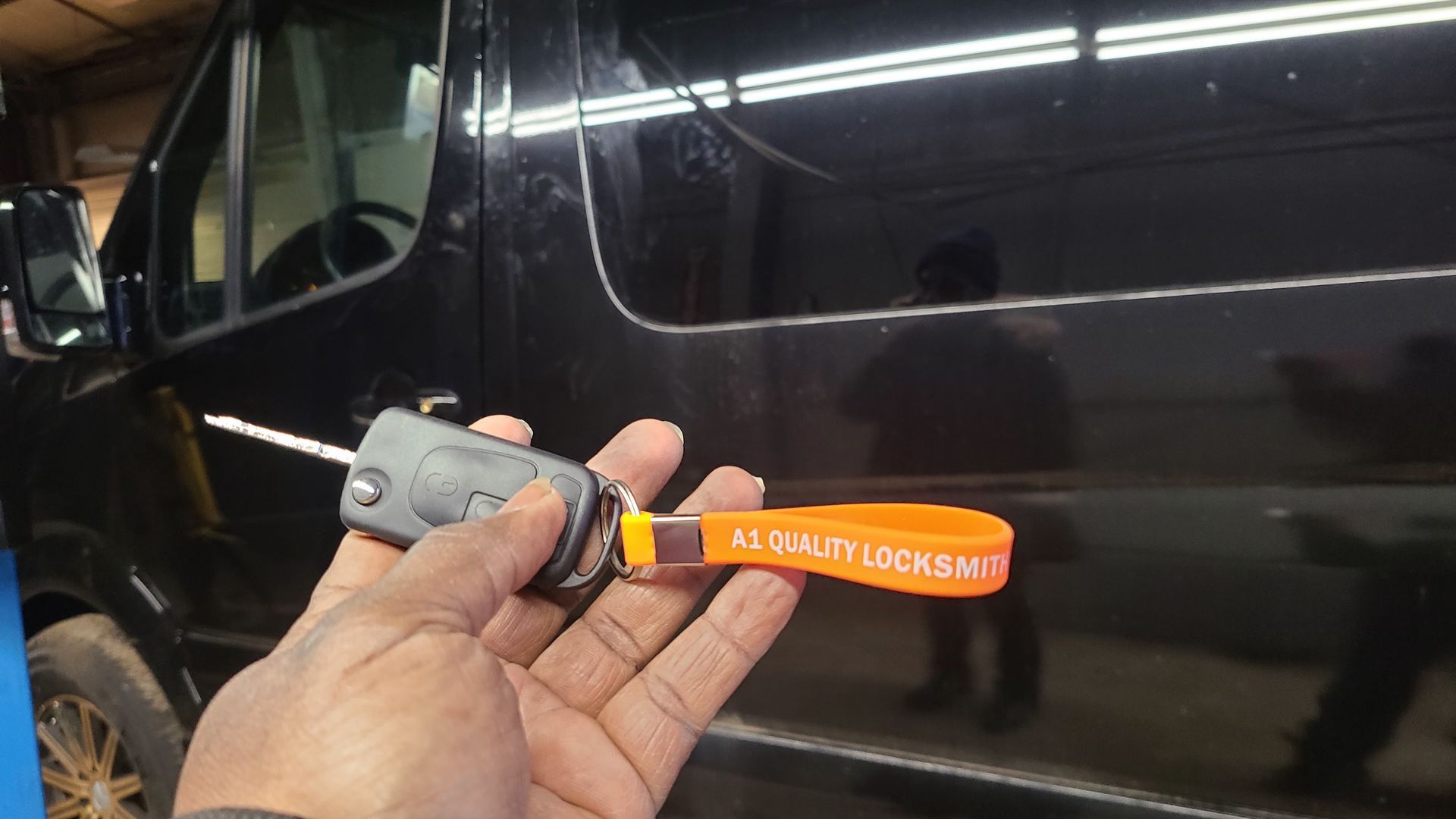 Hand holding a car key with orange tag in front of a black van. The tag says 