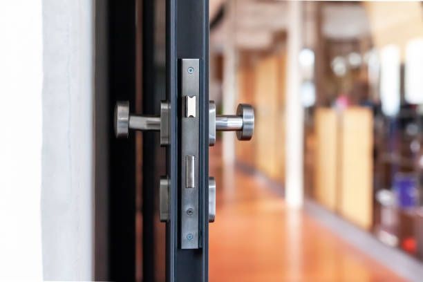 Door partially open, showing a metal lockset with handles, leading into a hallway with a wooden floor.