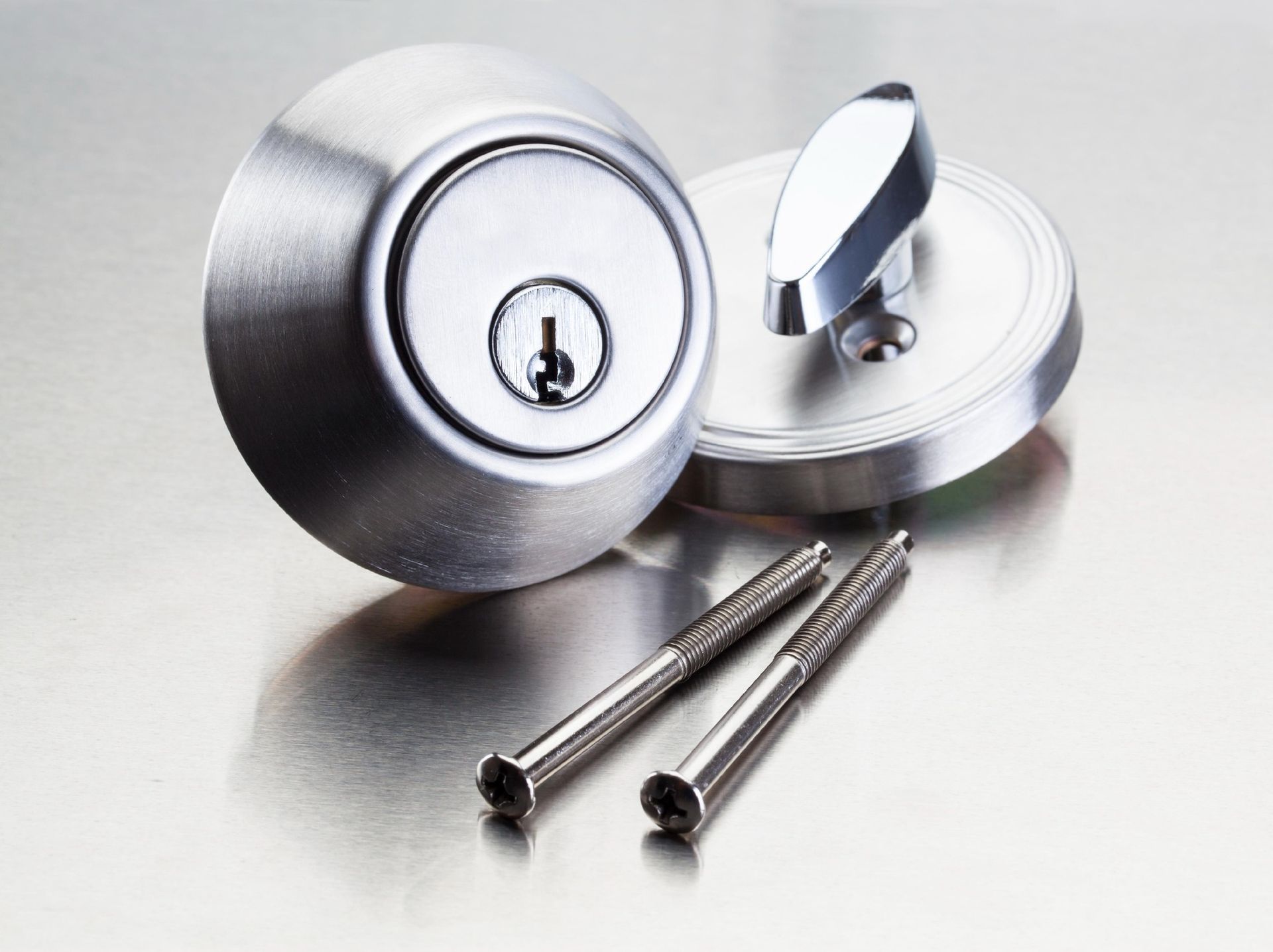 Close-up of a brushed metal deadbolt lock with a keyhole, handle, and two screws on a reflective surface.