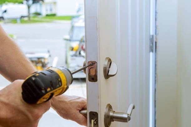 Person using a power drill to install a door latch on a white door.