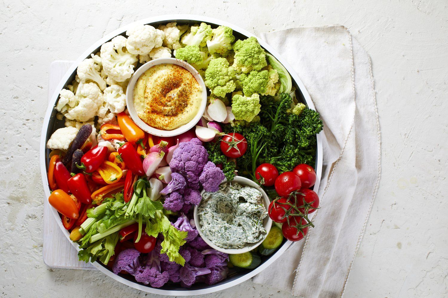 Vegetable platter: cauliflower, peppers, hummus, and dips on a white tray, beside a cloth. Food Stylist Nadine Page.