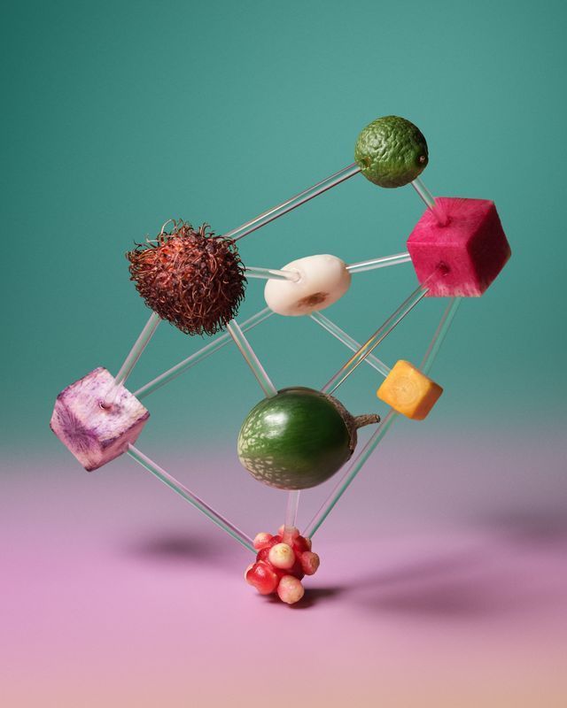 Colorful fruits and vegetables connected by wires, floating against a teal-pink gradient background. Food Stylist Nadine Page.