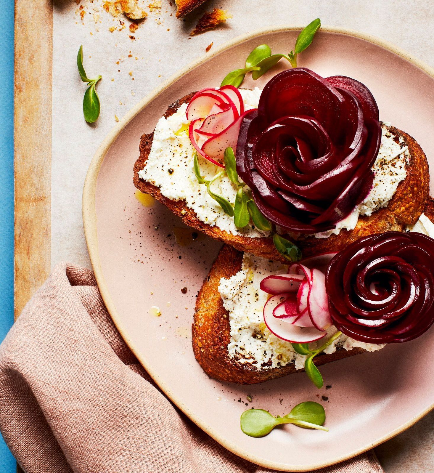 Two toasts topped with cheese and beet and radish roses on a pink plate. Food Stylist Nadine Page.