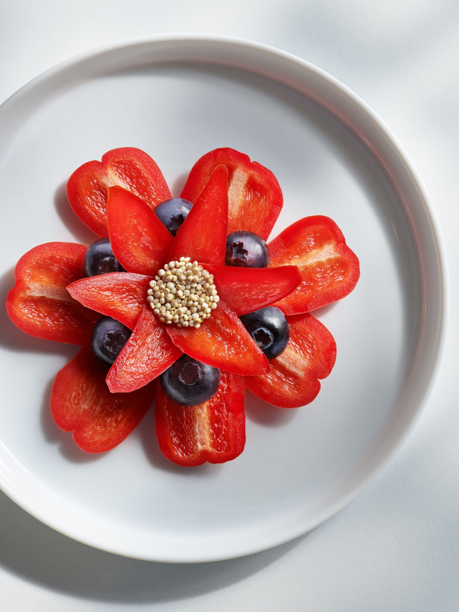 Red pepper slices and blueberries arranged in a flower shape on a white plate. Food Stylist Nadine Page.