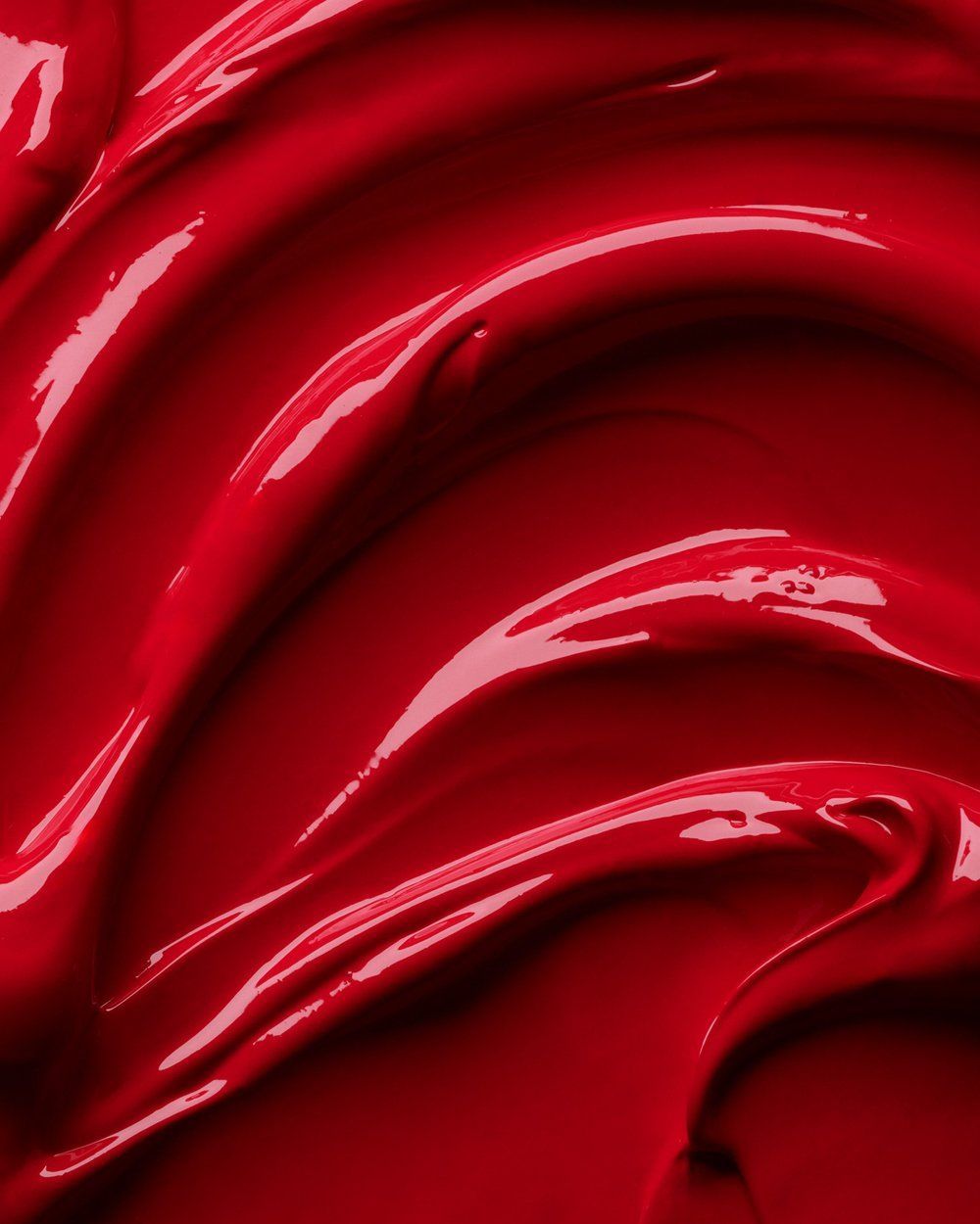 Abstract close-up of glossy red liquid paint with sweeping curved reflections