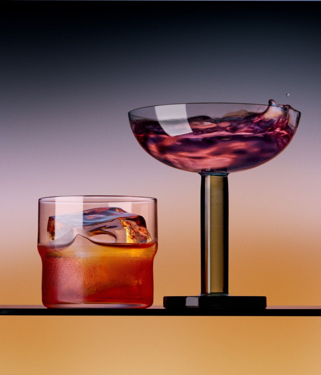 Two colorful cocktail glasses on a bar, one low and one on a stem against a gradient background