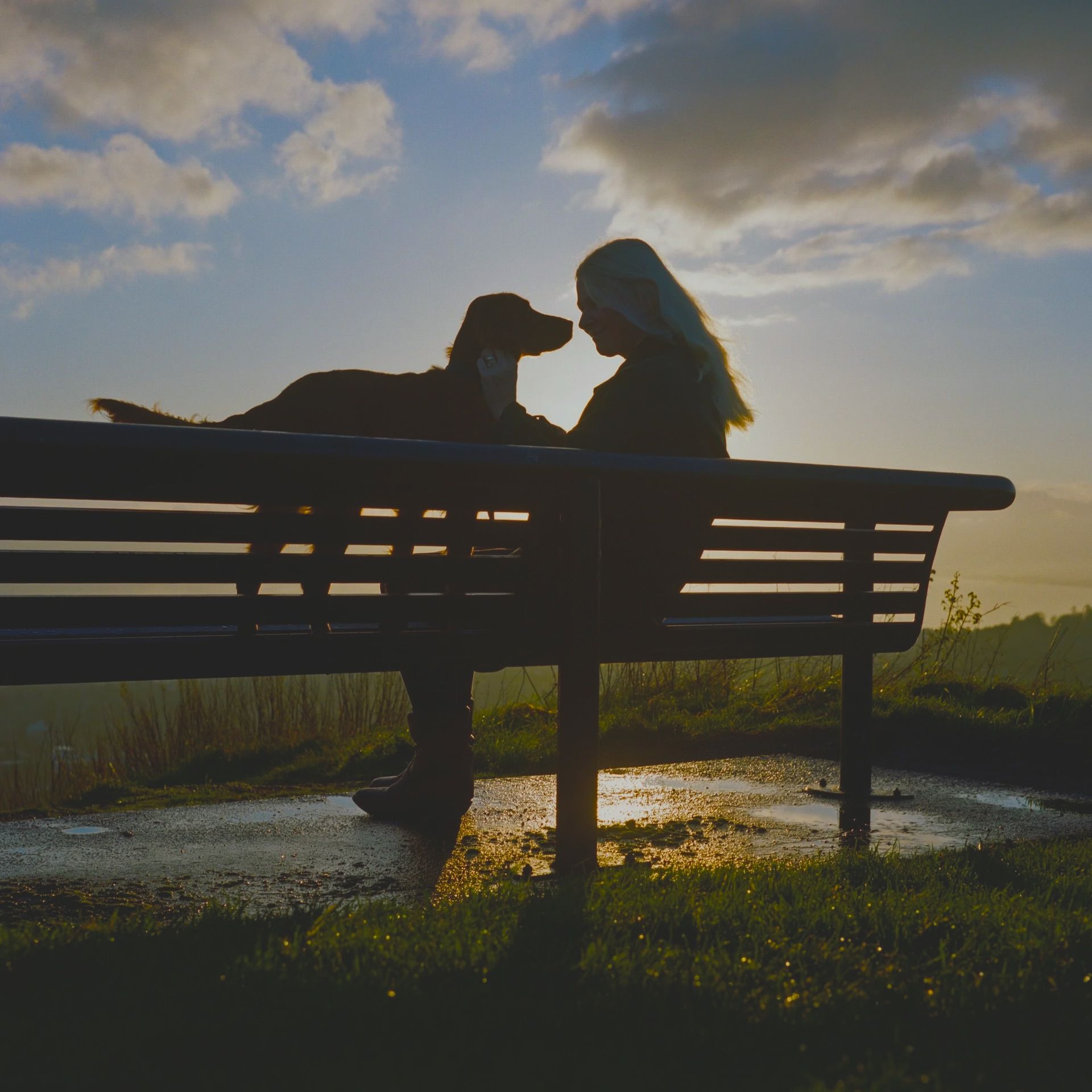 Woman looks at her dog directly on a park bench