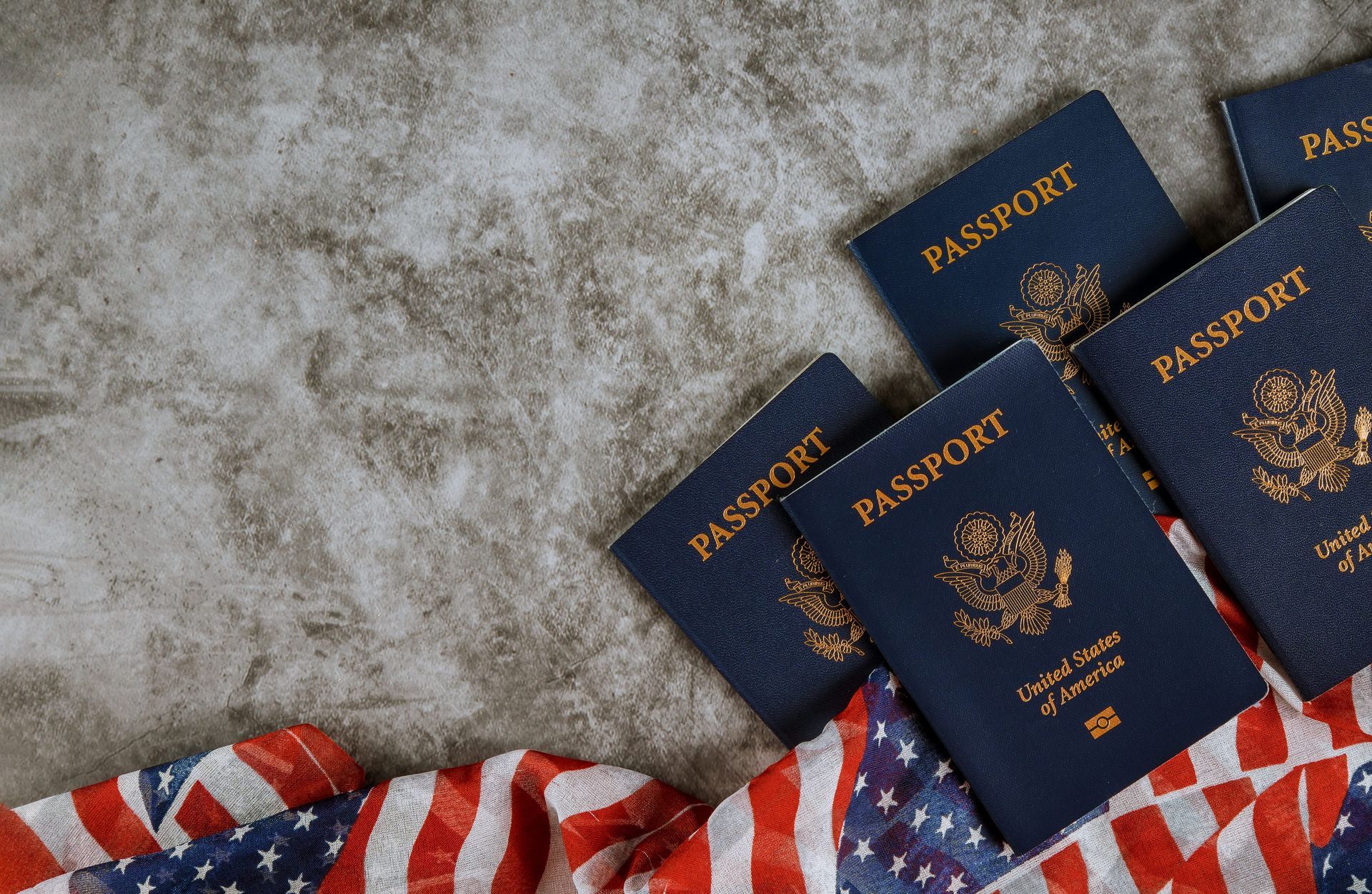 Several blue passports on a gray surface beside a red, white, and blue cloth.