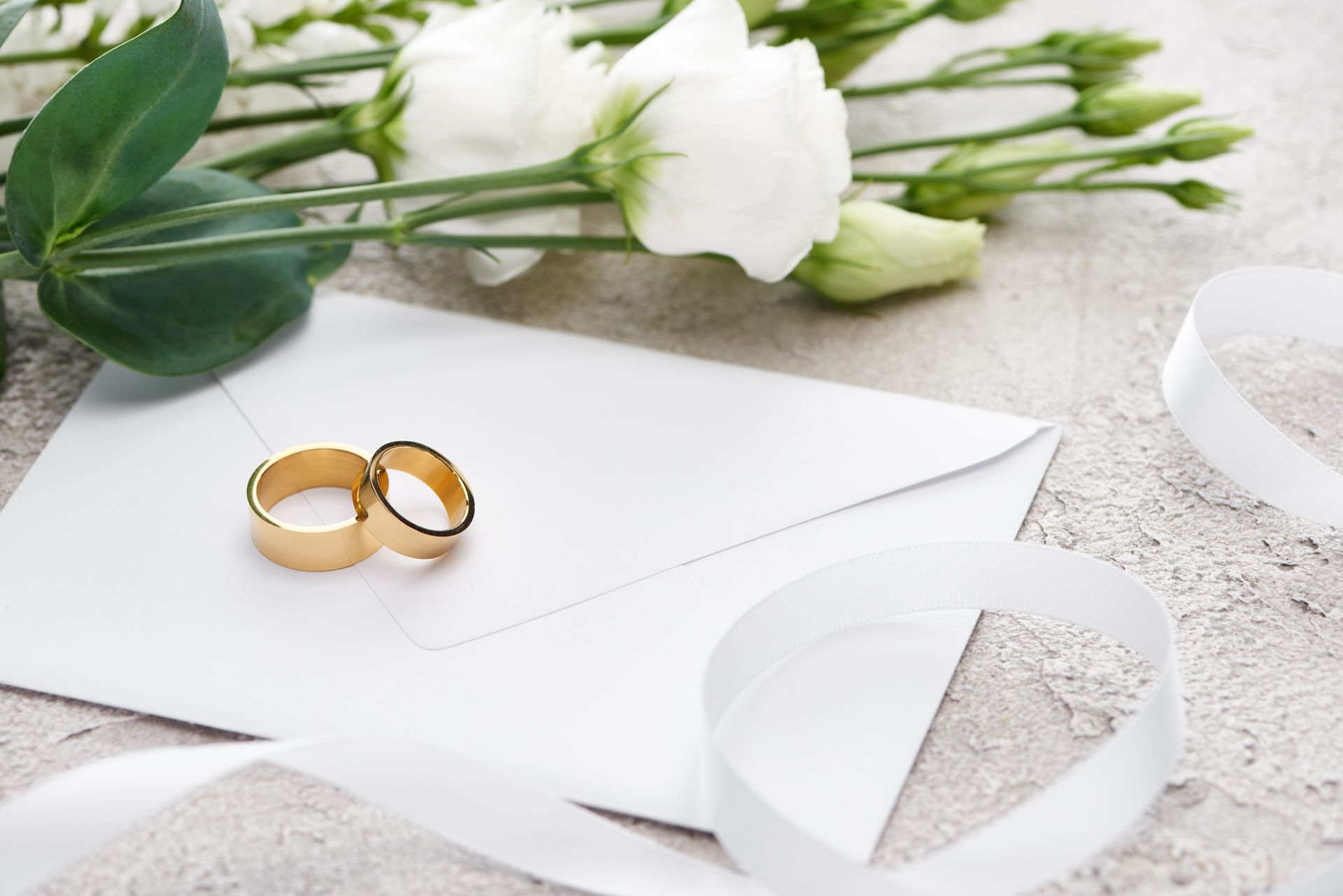 Wedding rings on a white envelope with white flowers and a ribbon