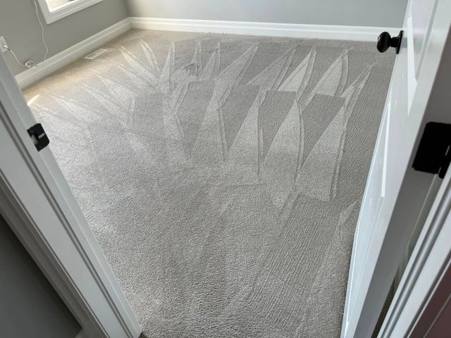 Empty gray-carpeted room with white walls and an open door view.