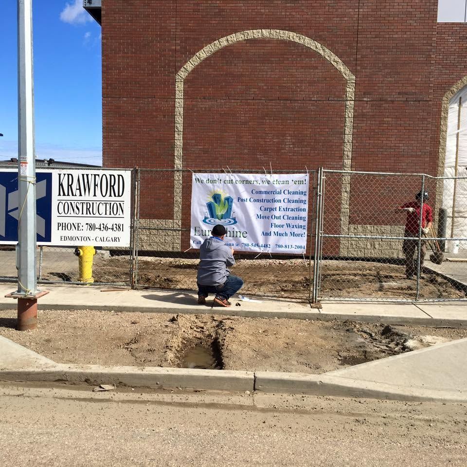 Person kneels by a fence in front of a brick building and a Crawford Construction sign.