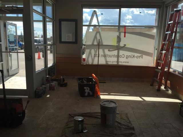 Empty storefront interior with construction tools, ladders, and a large front window covered in protective film.