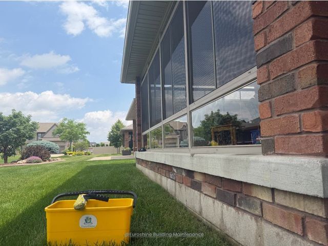 Yellow recycling bin beside a brick building with reflective windows and a grassy lawn under a blue sky