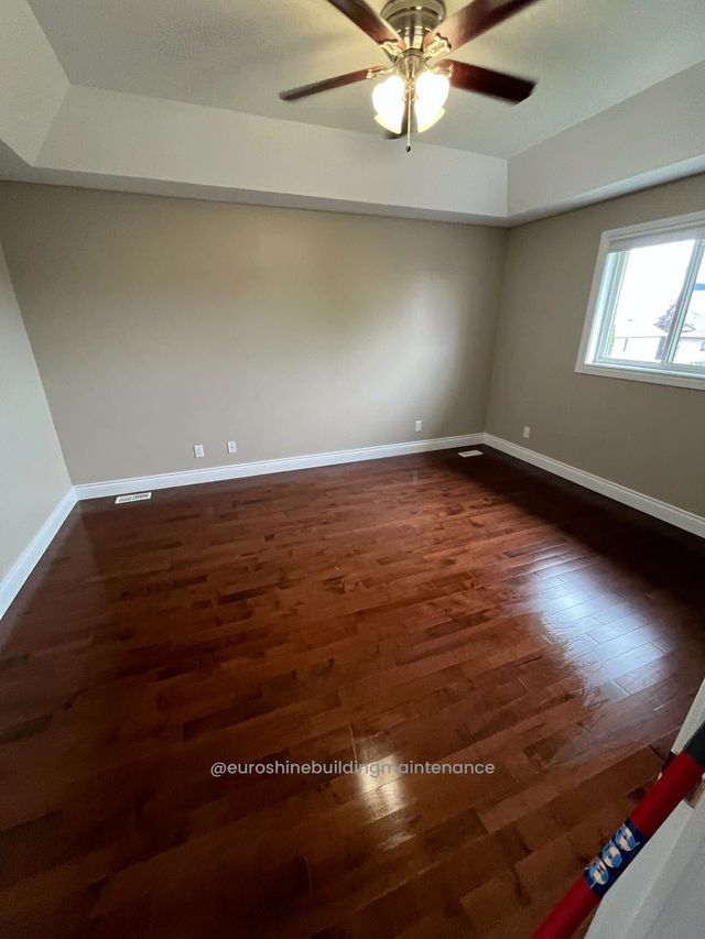 Empty room with glossy hardwood floor, beige walls, ceiling fan, and a window.