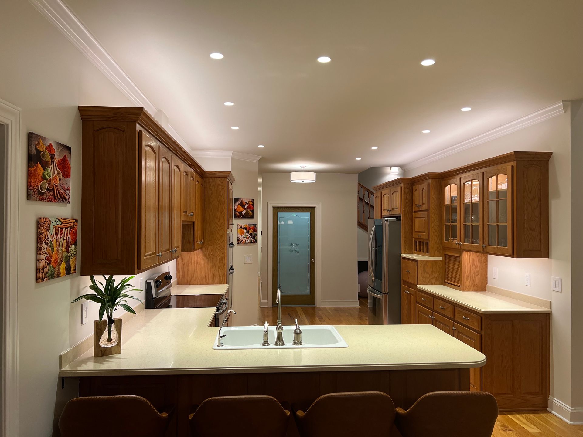 Kitchen with light wood cabinets, white countertops, and recessed lighting. Island with bar stools.