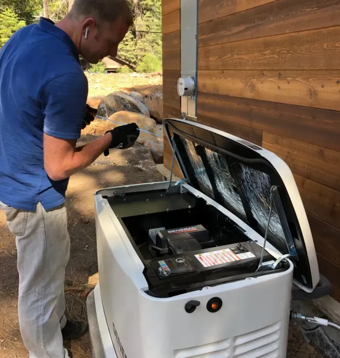 Man inspecting electrical panel with yellow device; indoor setting. Man working on a white generator outside a building with brown siding. The generator's lid is open.